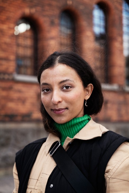 Tahiya Niskala, a copywriting student at Berghs School of Communication, poses in front of the school's red brick building with arched windows.
