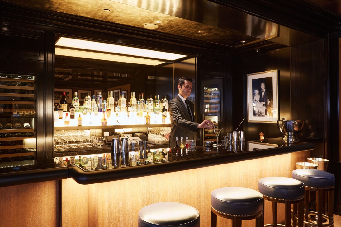Professional bartender in dark suit preparing drinks behind illuminated bar with extensive bottle display at Fasano