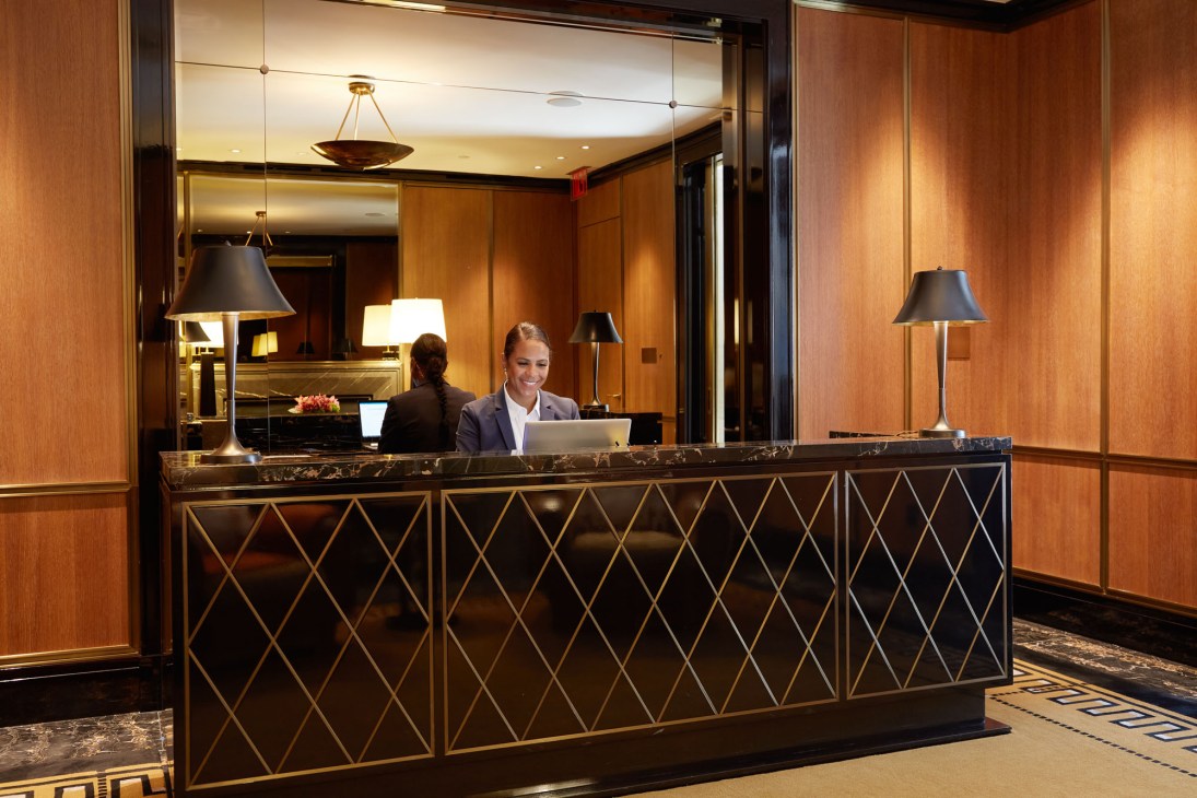 Hotel reception desk with staff member in professional attire working at computer in elegant wood-paneled lobby