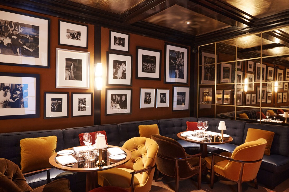 Elegant restaurant interior with mustard velvet chairs, dark banquettes, framed photographs and intimate table settings