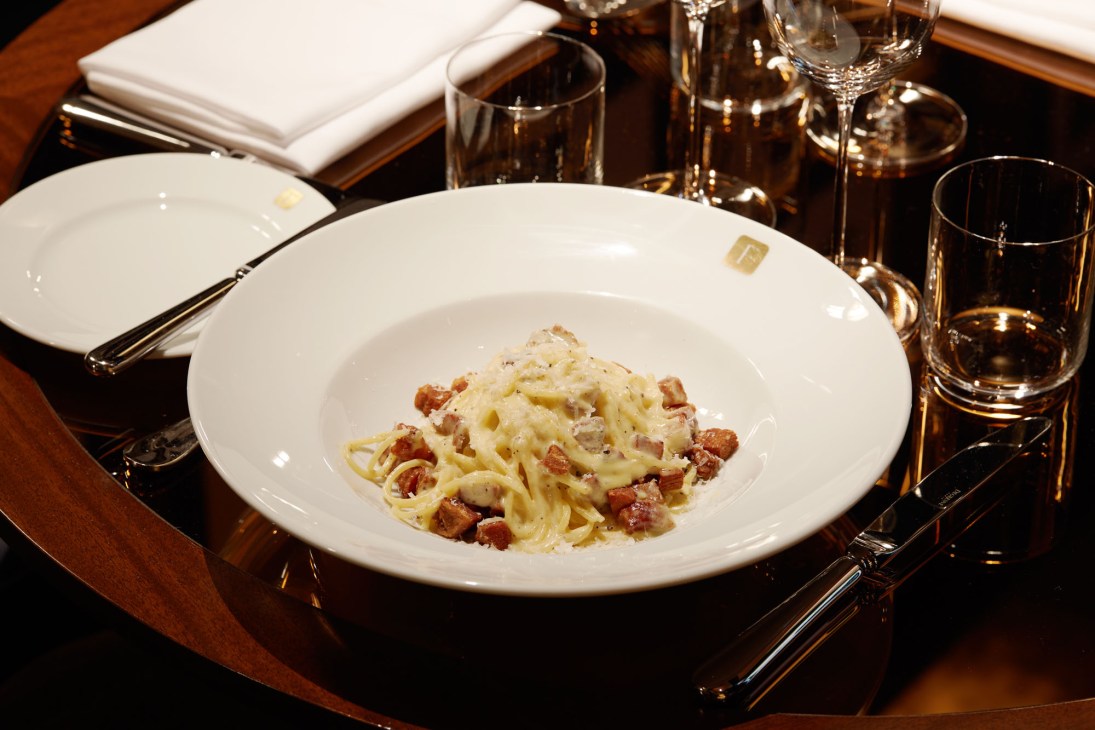 Pasta dish with bacon and cheese served in white bowl on elegant table setting with glassware