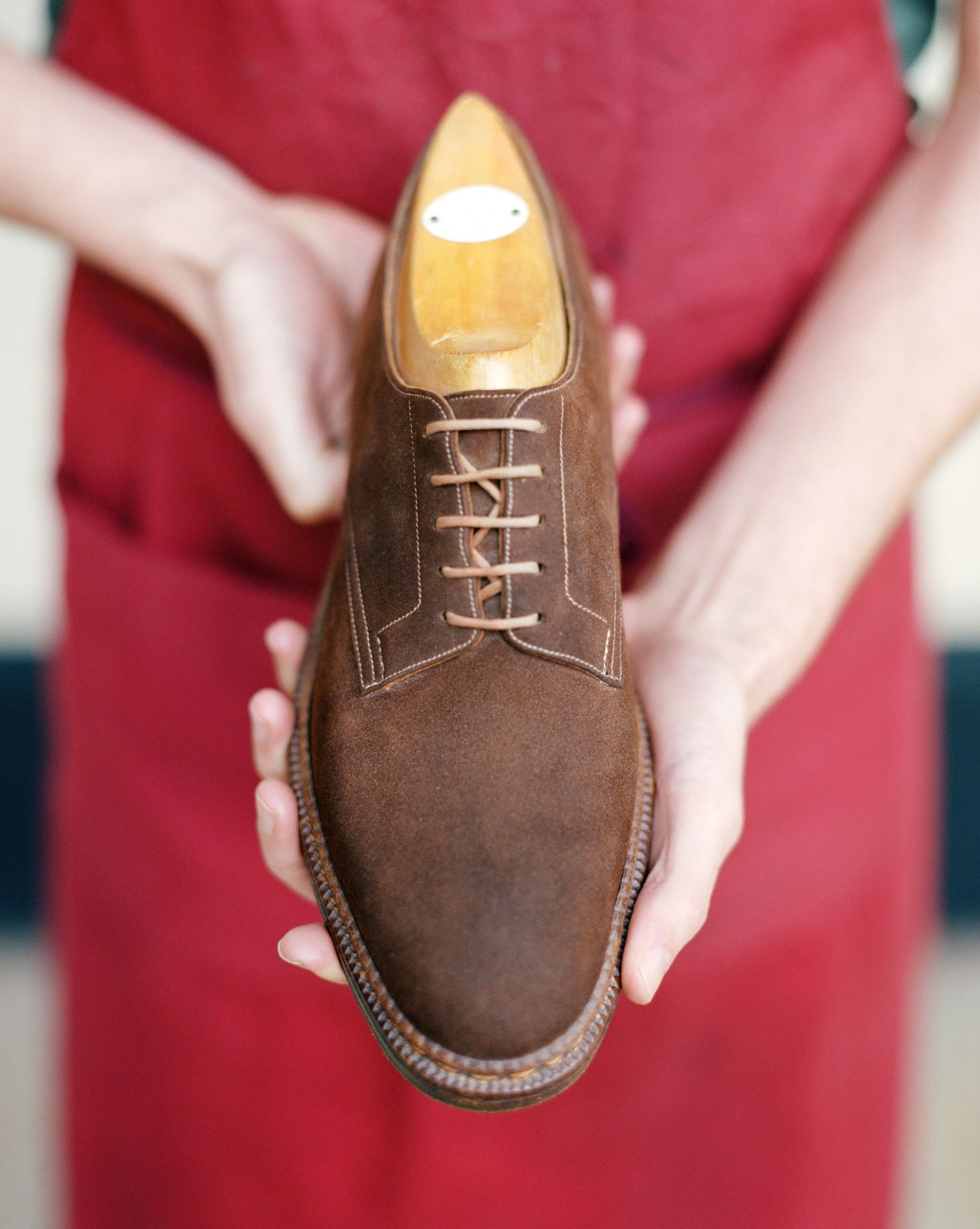 Brown suede dress shoe with laces held in cupped hands against red background