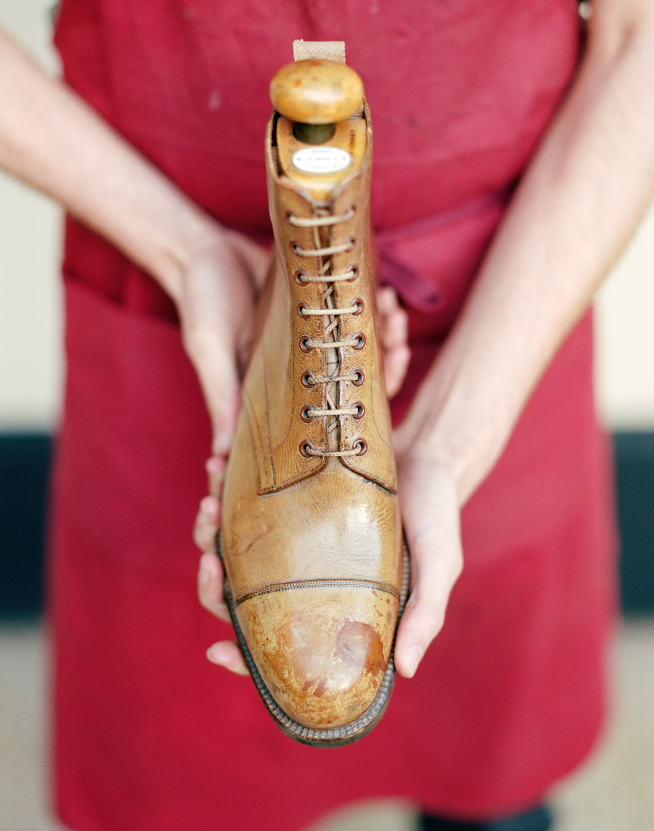 Person in red shirt holding vintage brown leather boot with laces between their hands