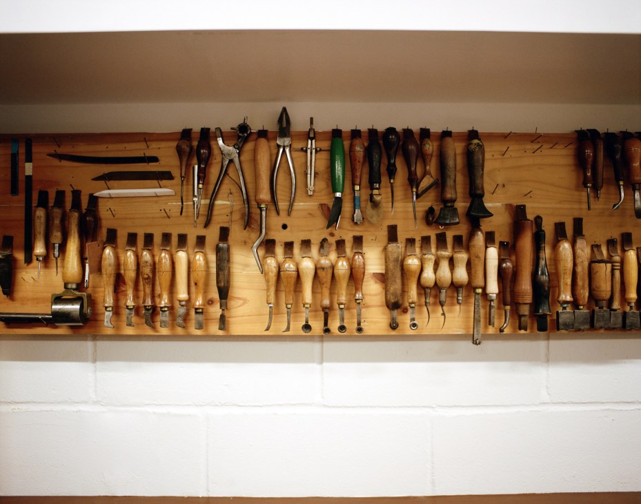 Traditional shoemaking tools with wooden handles arranged on a wooden workbench