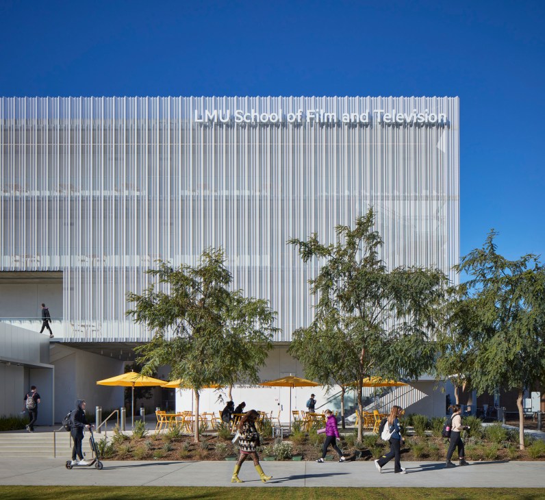 Modern university building with vertical metal cladding and students walking outside with yellow umbrellas
