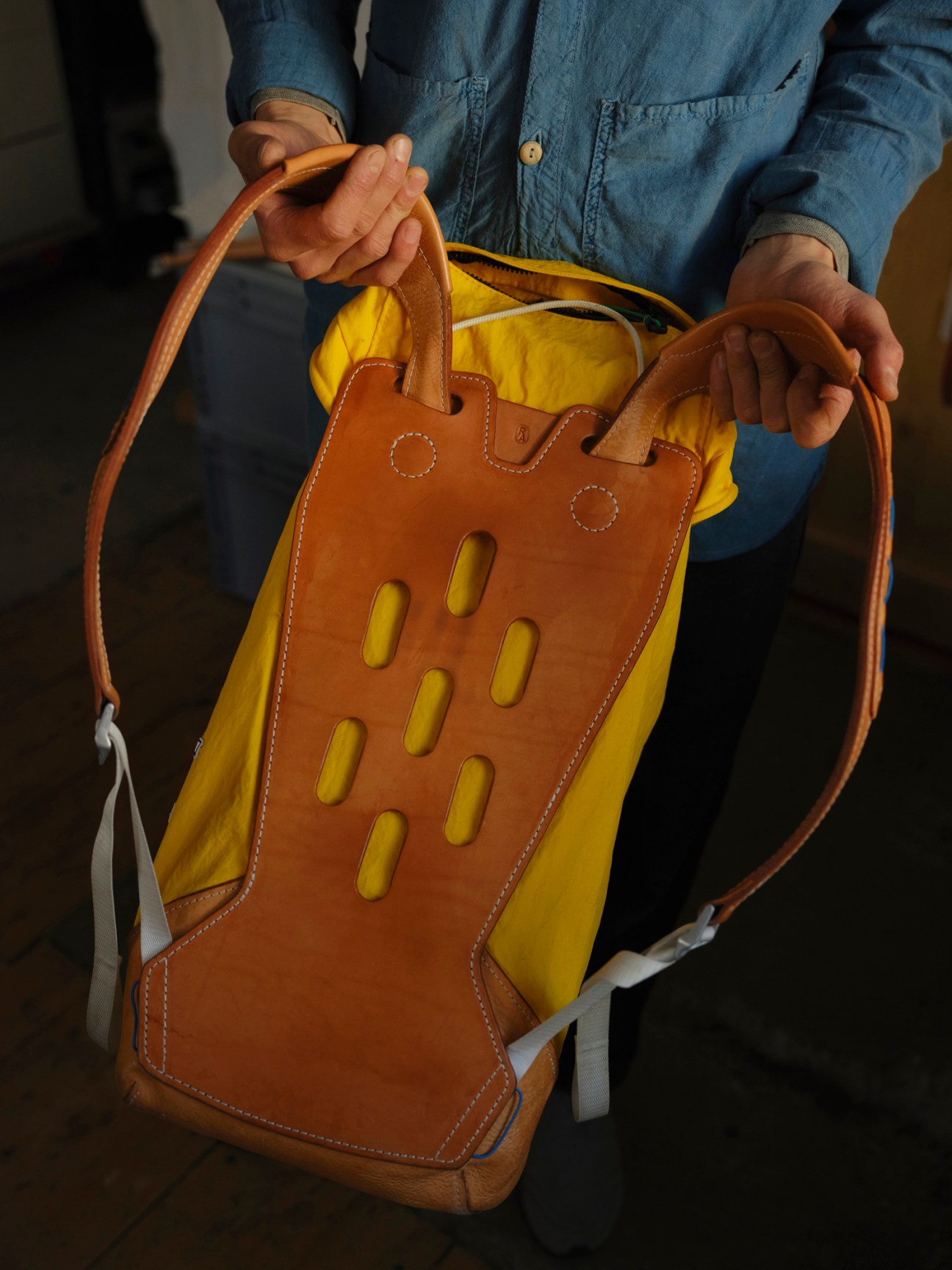 Person holding a brown leather Racing Atelier backpack with yellow interior and oval cutout details