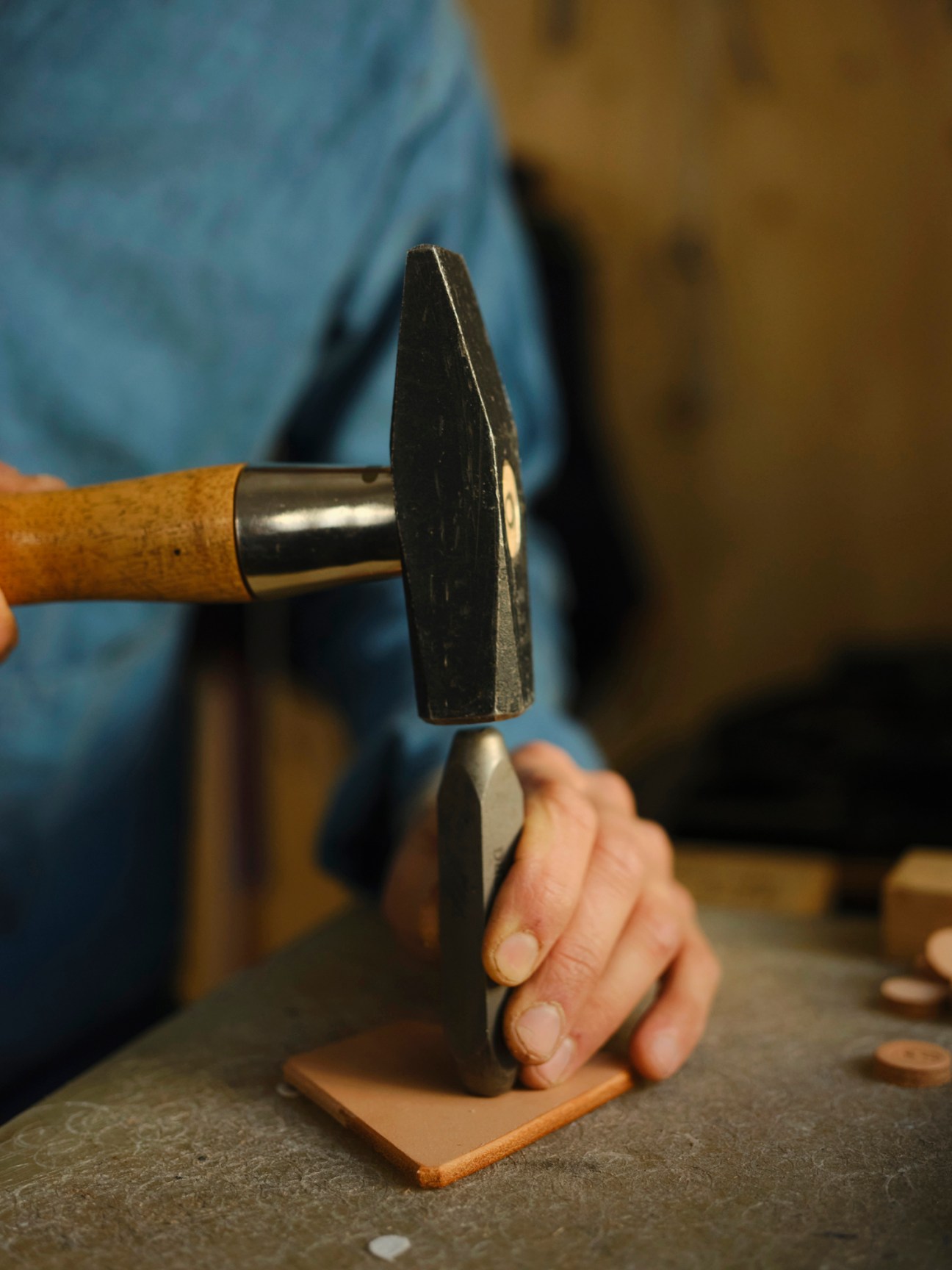 Hand using hammer and punch tool to emboss Racing Atelier logo onto leather