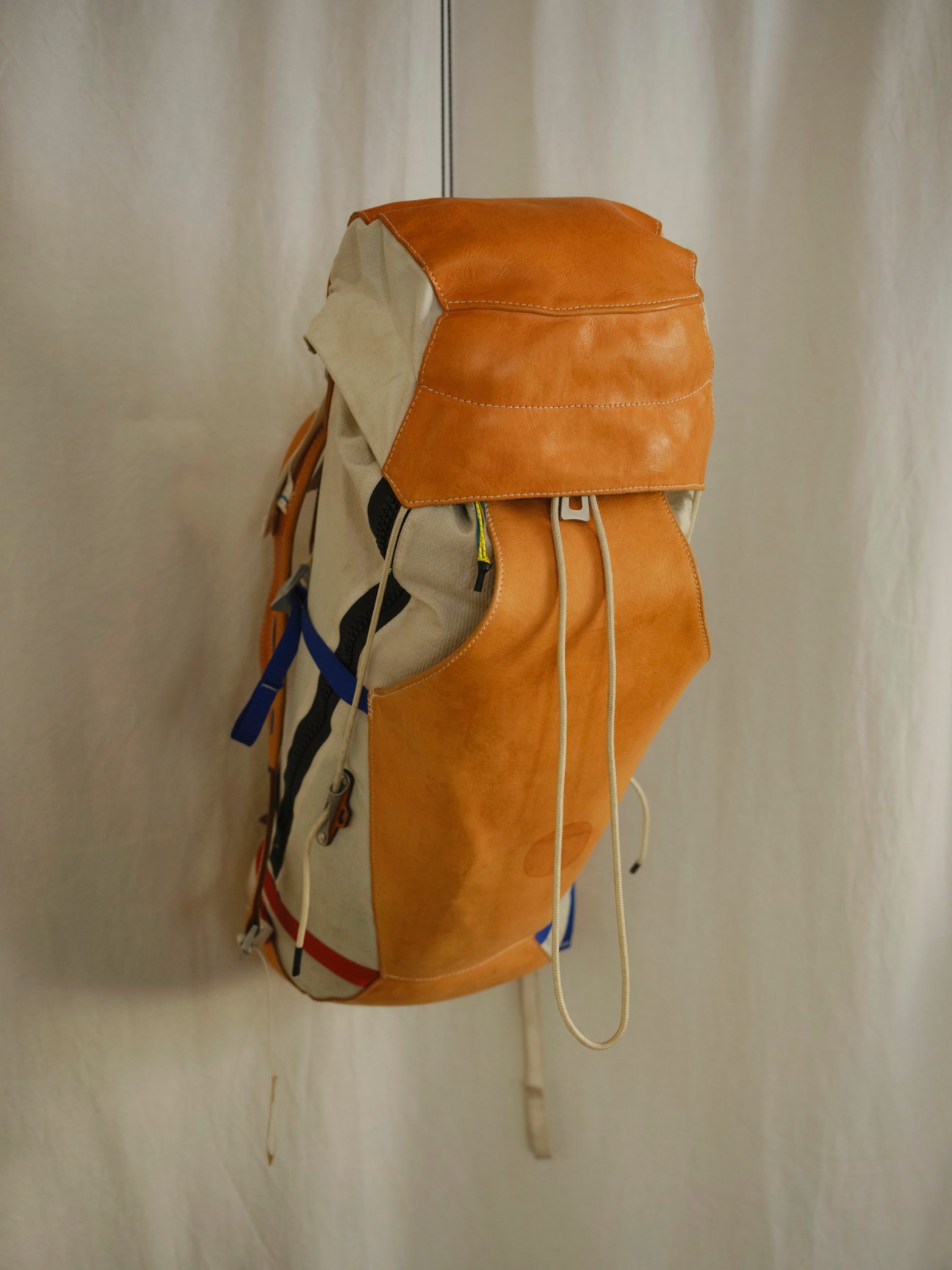 Racing Atelier backpack with tan leather construction and colorful fabric panels hanging against neutral background