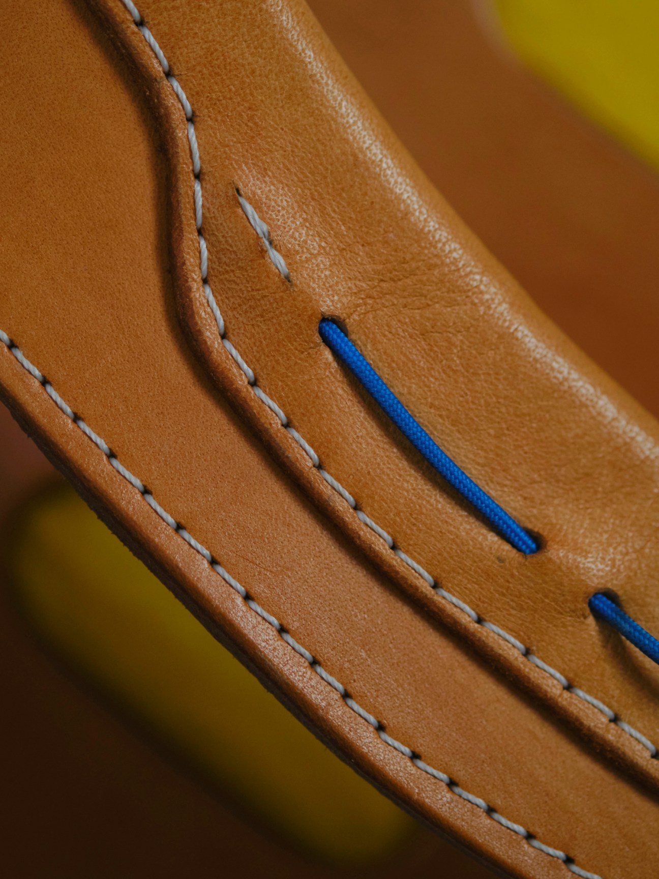 Close-up of tan leather bag straps with blue cord threading and decorative stitching