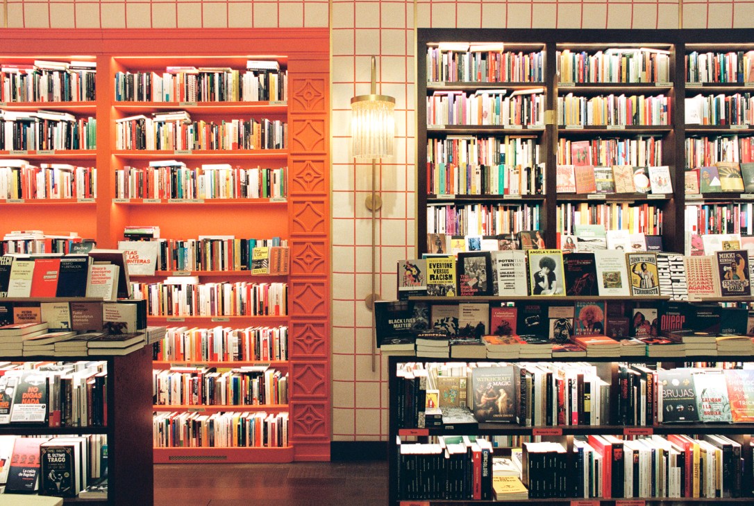Interior of Llibreria Finestres bookshop with orange and black bookshelves filled with books and display tables