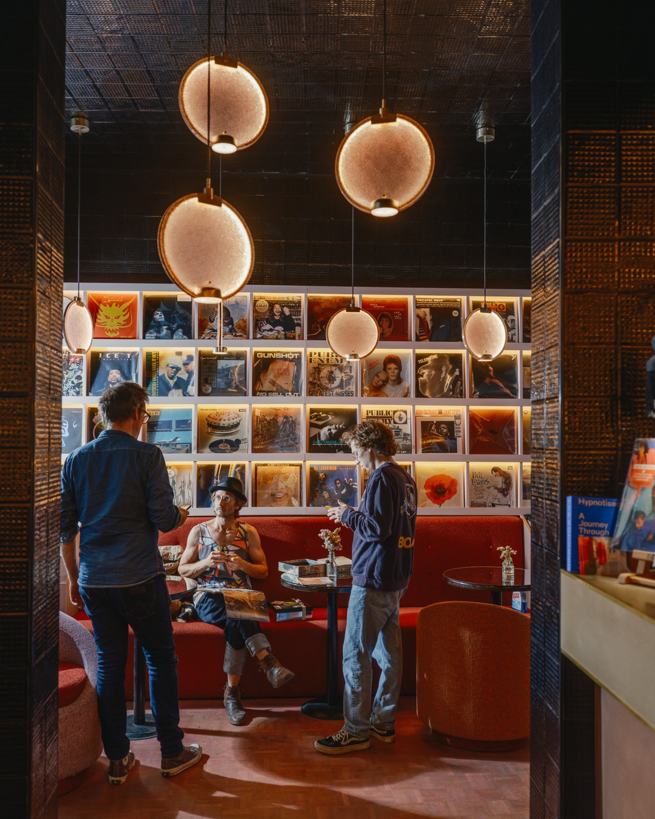 Three people socializing in a record store with vinyl albums displayed on wall and pendant lighting