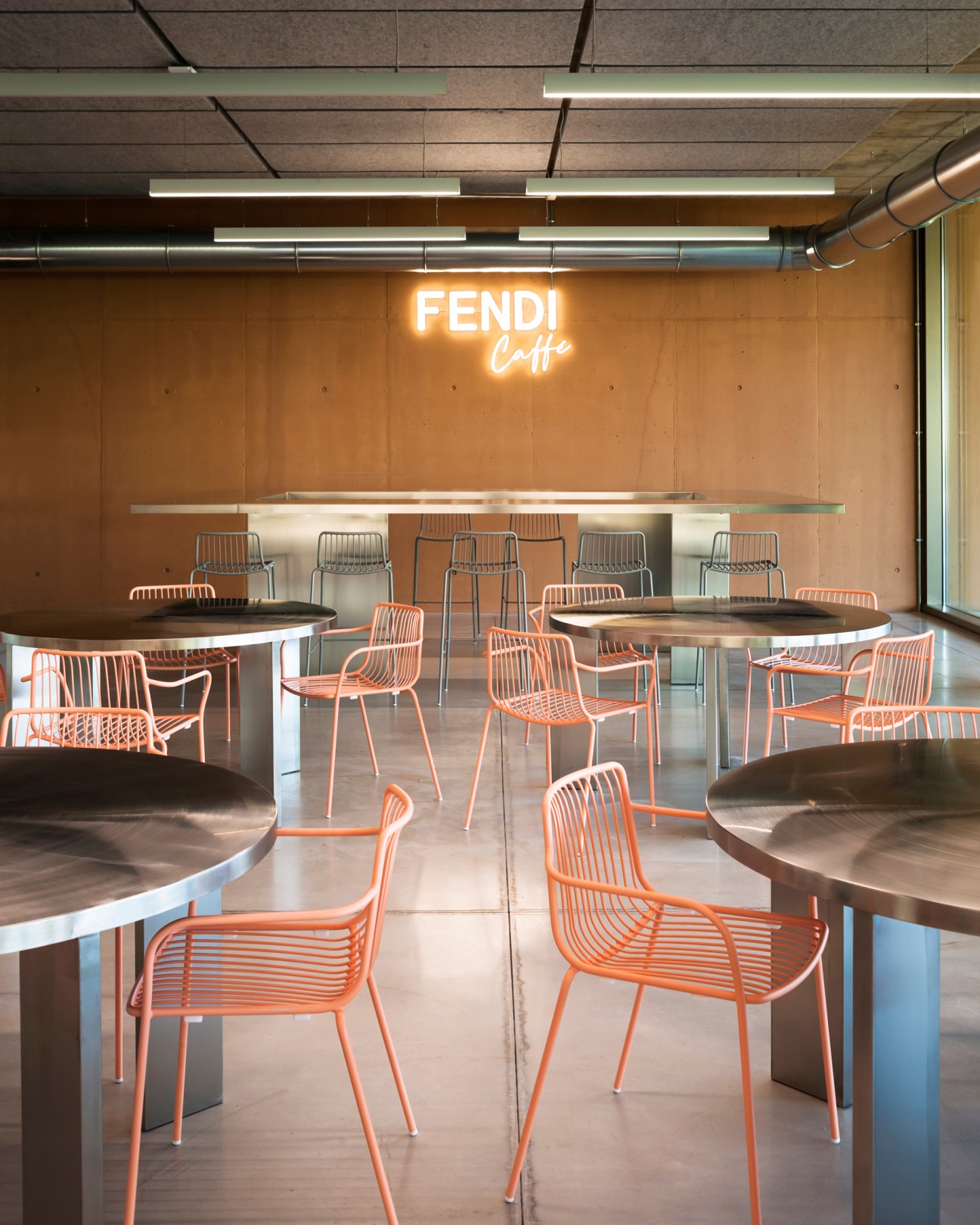 Modern cafe interior with orange wire chairs, round tables, and illuminated Fendi Caffe neon sign on brown wall