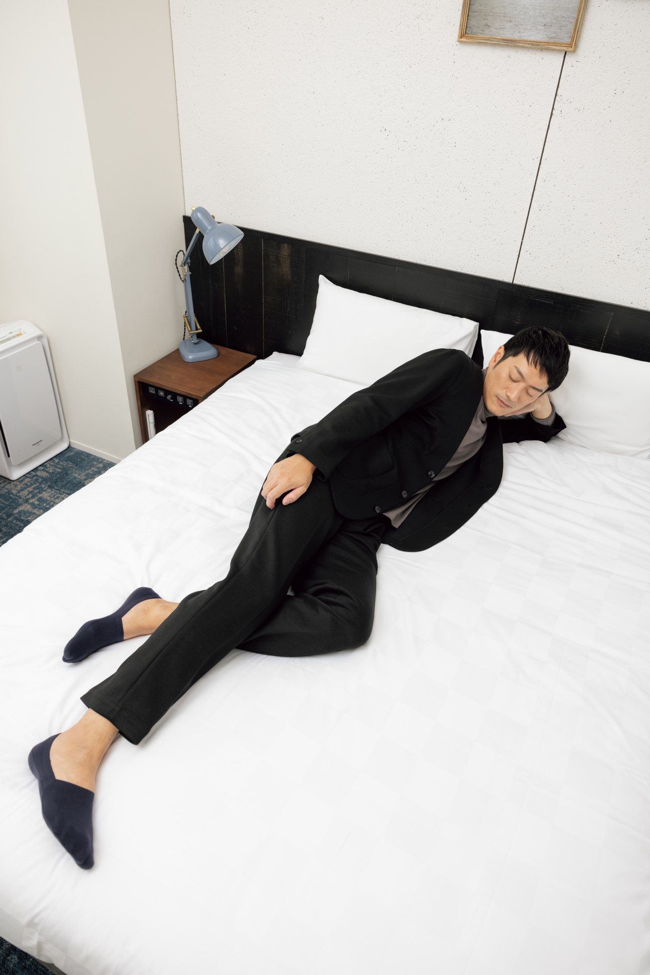 Person in dark business suit lying on hotel bed in relaxed position