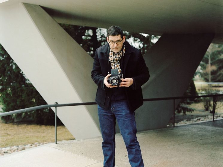Felix Brüggemann holding camera while standing under modern concrete architecture in Berlin
