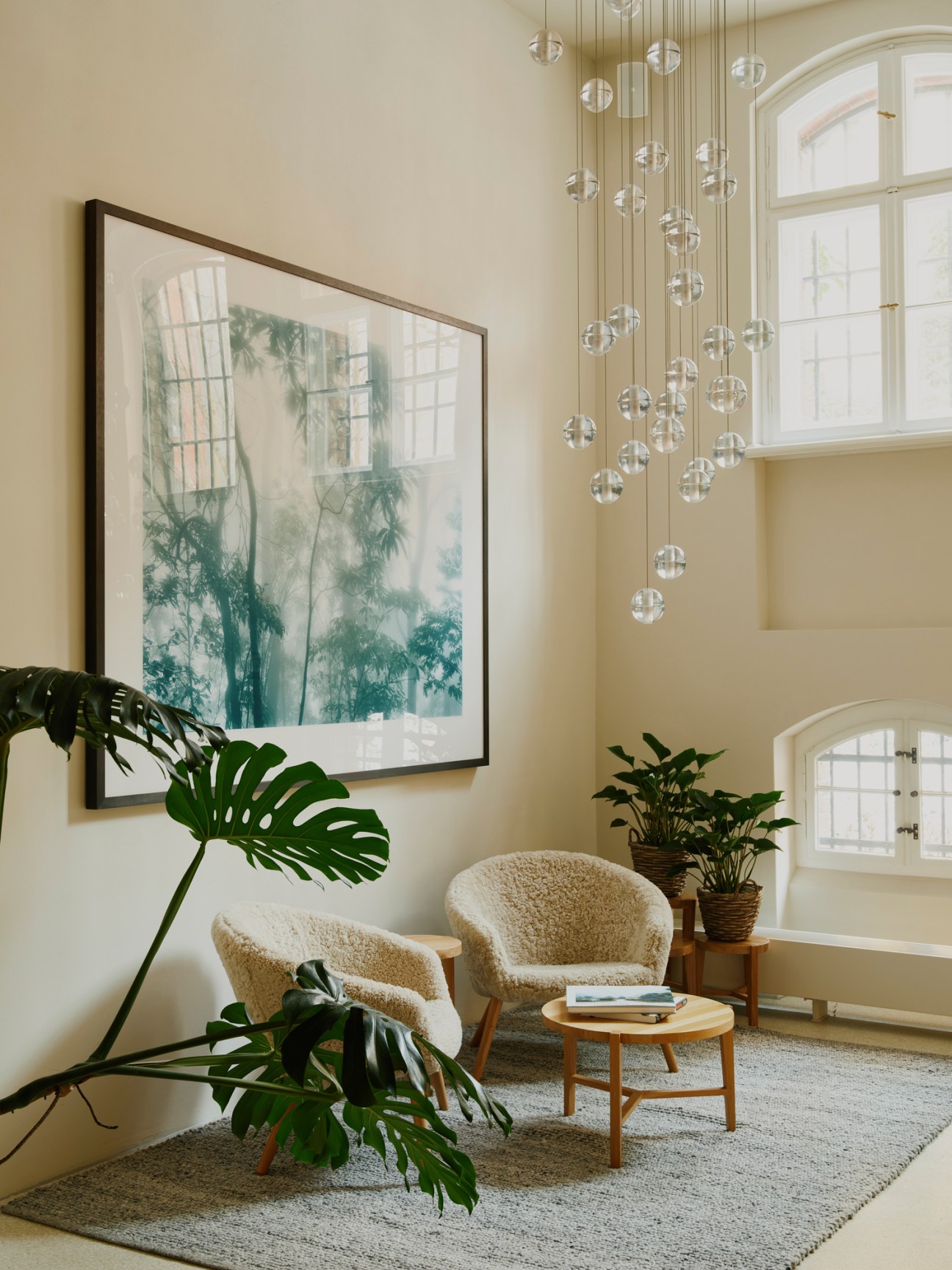 Modern hotel seating area with two textured chairs, glass orb chandelier, botanical artwork, and plants