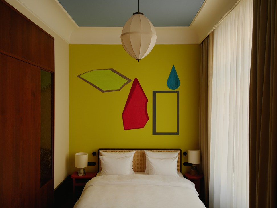 Château Royal Berlin bedroom with vibrant yellow accent wall, geometric wall art, and modern pendant lighting