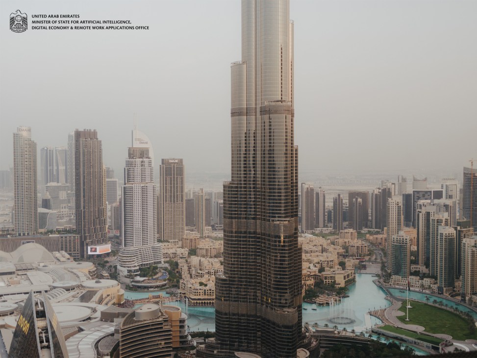 Dubai skyline with high-rise towers and turquoise waterway, featuring UAE AI Office branding.