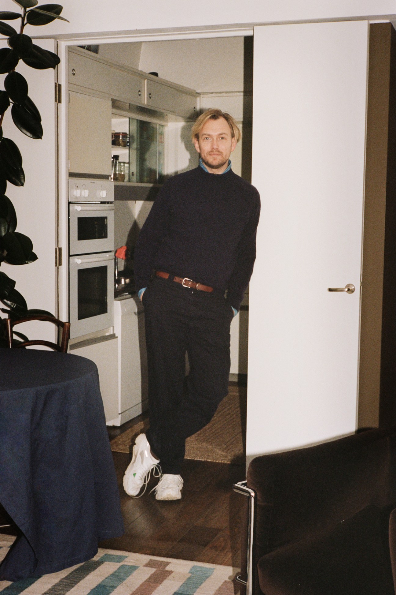 Tom Morris stands in a modern kitchen doorway wearing a black turtleneck and dark trousers