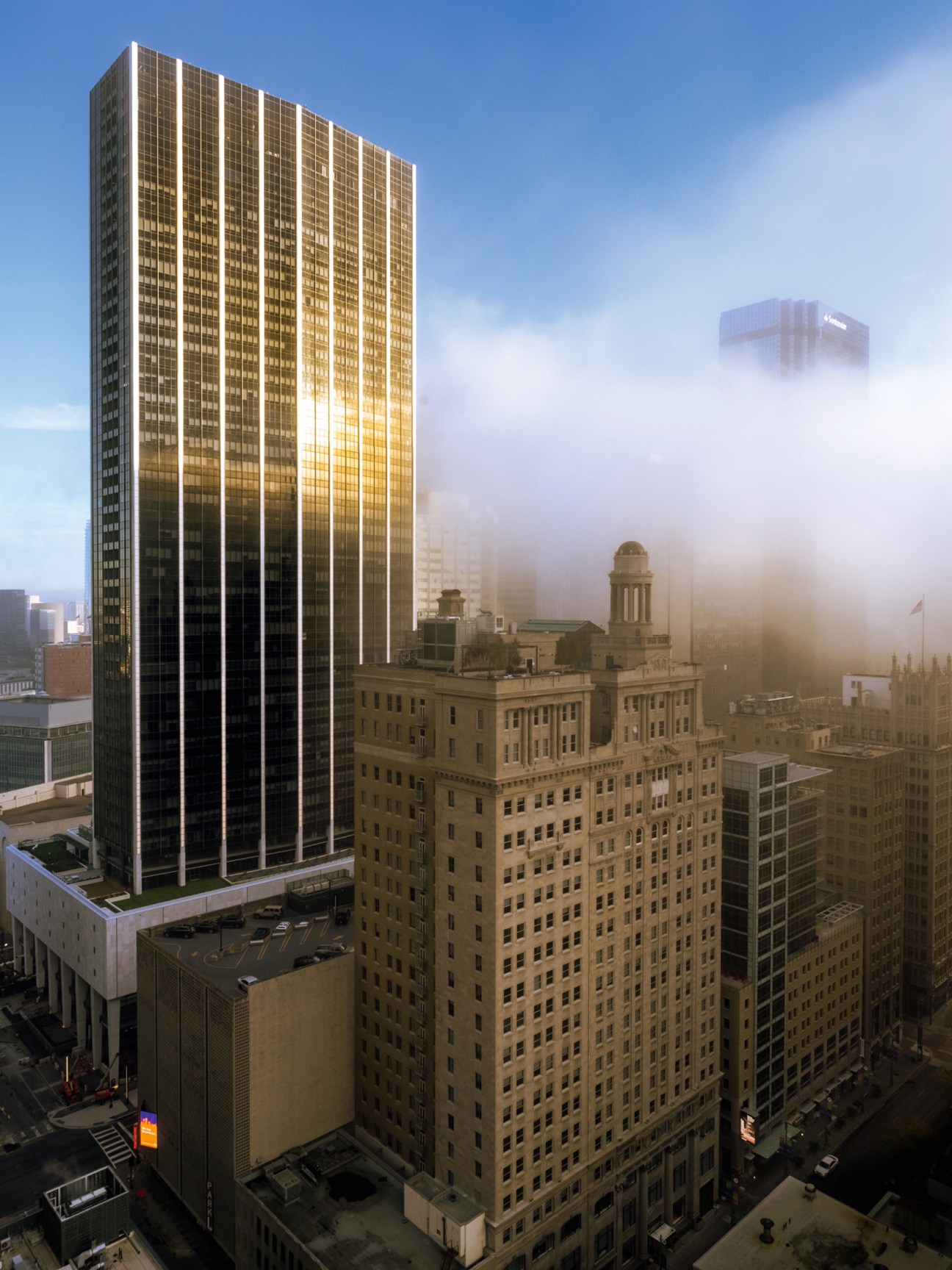 Modern glass skyscraper rising above historic downtown Dallas buildings shrouded in fog