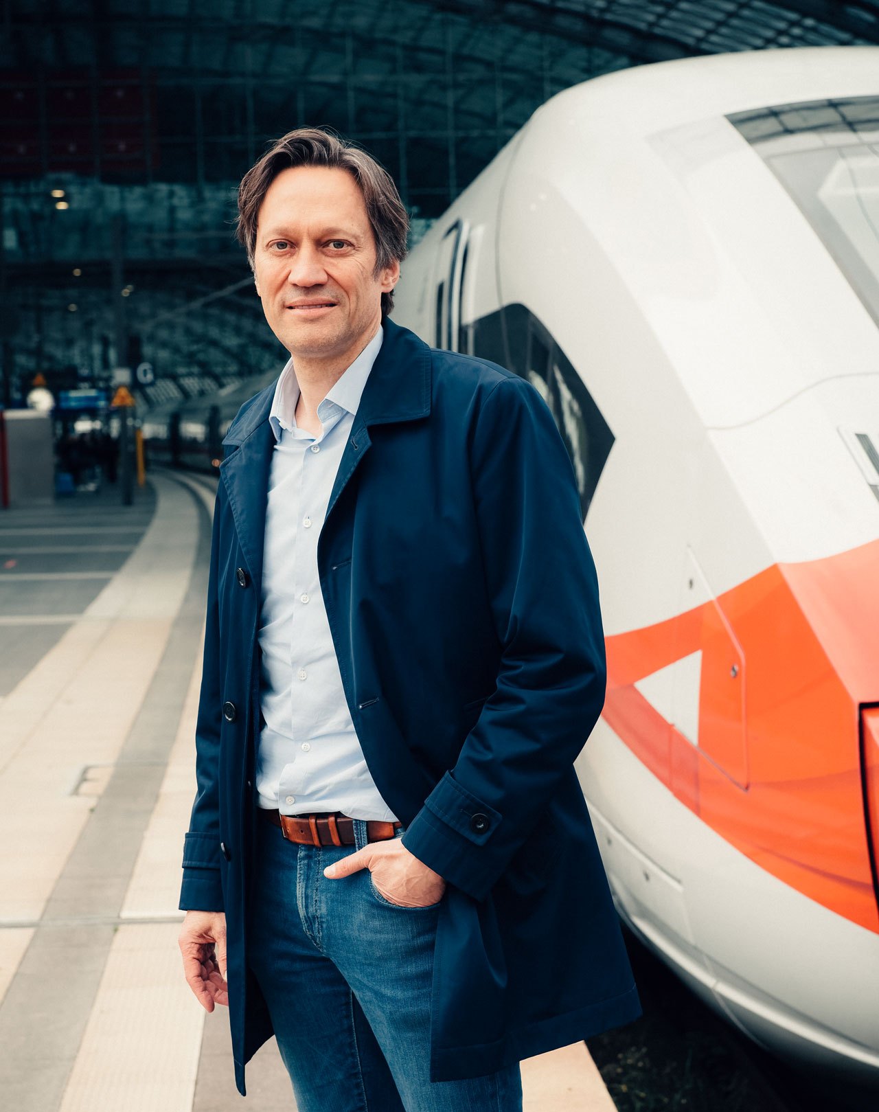 Michael Peter, CEO of Siemens Mobility, standing beside a white and orange high-speed train in a modern station