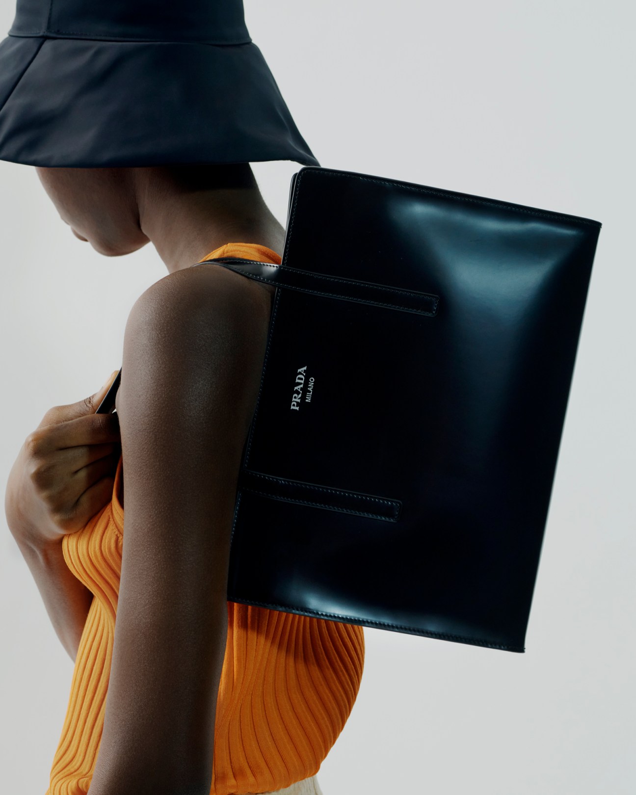 Person wearing yellow ribbed cardigan and black skirt holding large black leather Prada bag
