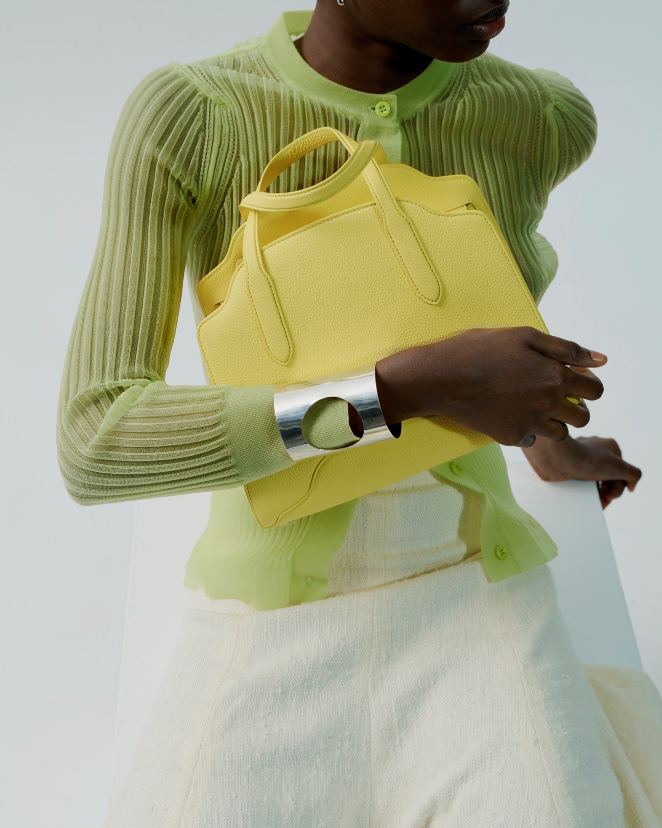 Model wearing lime green Cecilie Bahnsen cardigan, Chloé skirt, holding yellow Loro Piana bag and silver cuff
