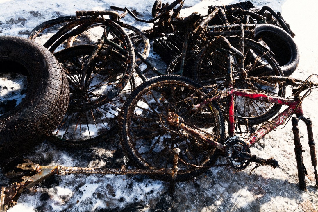 Collection of retrieved bicycles and car tyres laid out on snowy ground after being pulled from underwater
