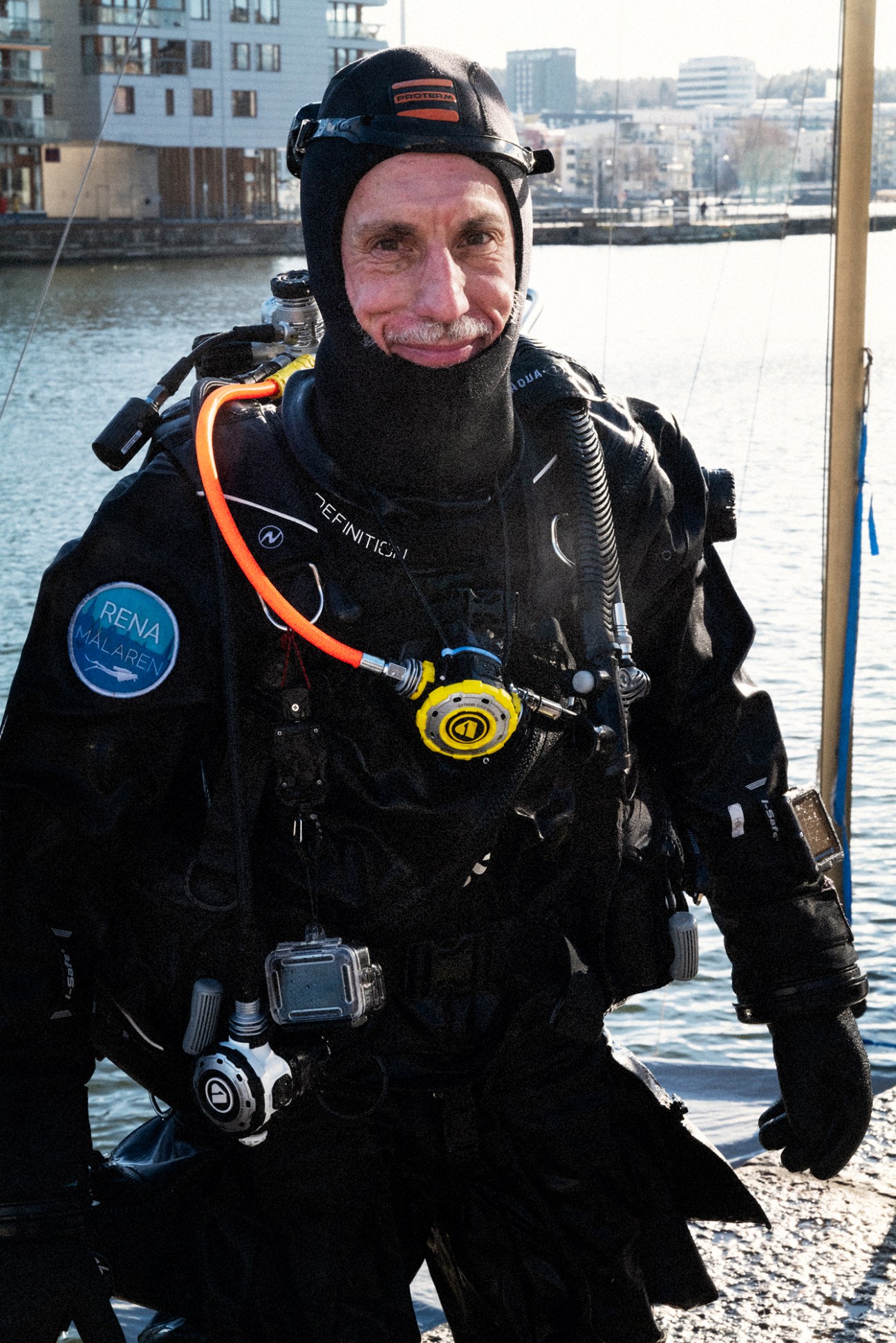 Volunteer Oskar Kihlborg in diving gear with oxygen tanks standing beside a canal in Stockholm