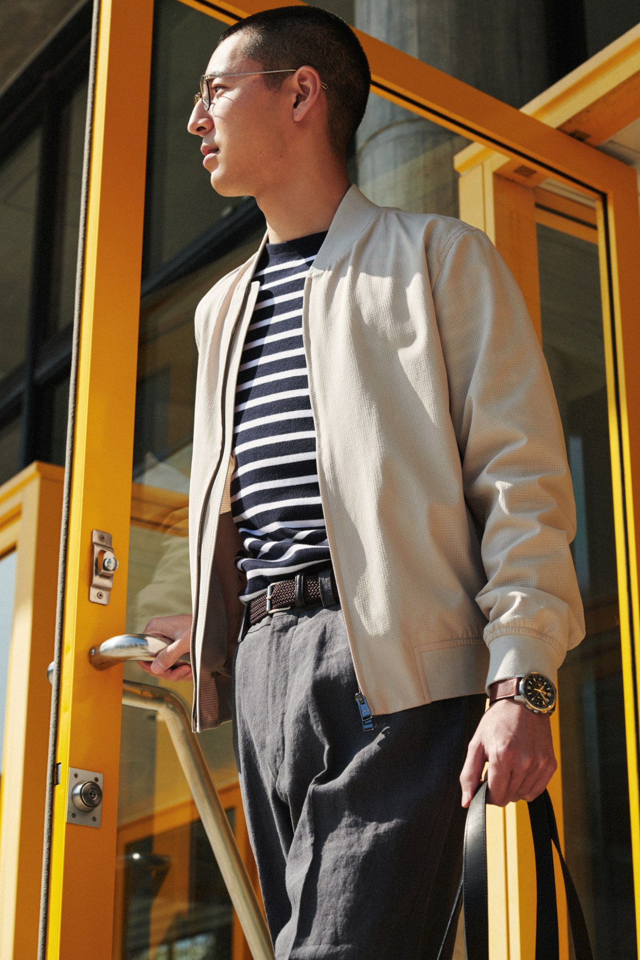 Man in beige bomber jacket and striped shirt standing by yellow door
