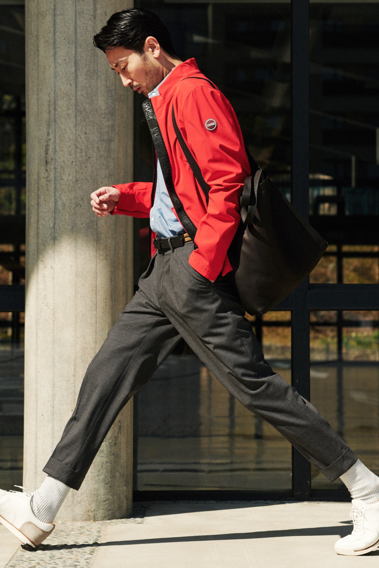 Man in red Colmar jacket and grey trousers walking with messenger bag