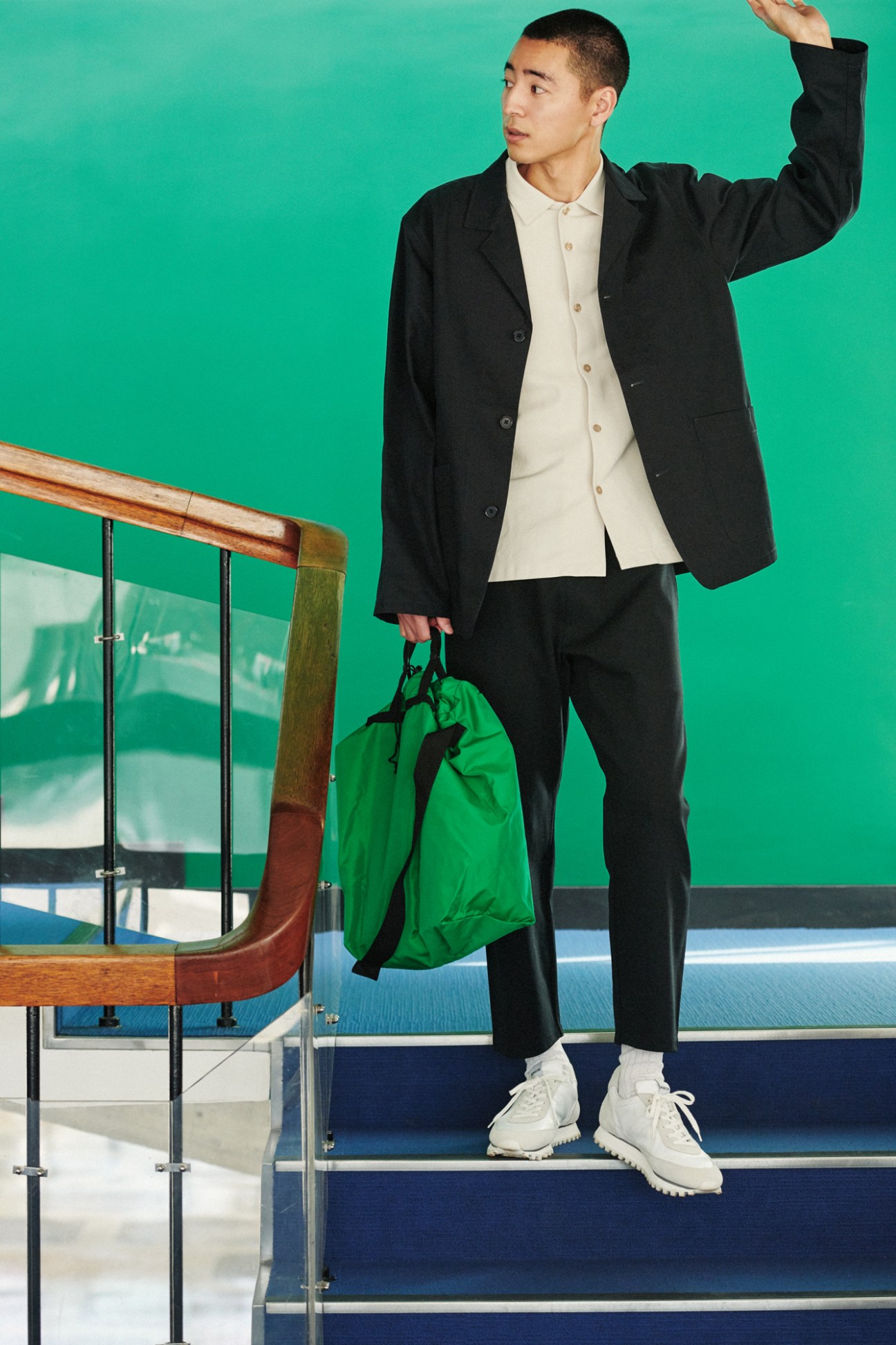Man in black jacket and cream shirt holding green bag on stairs with glass railing