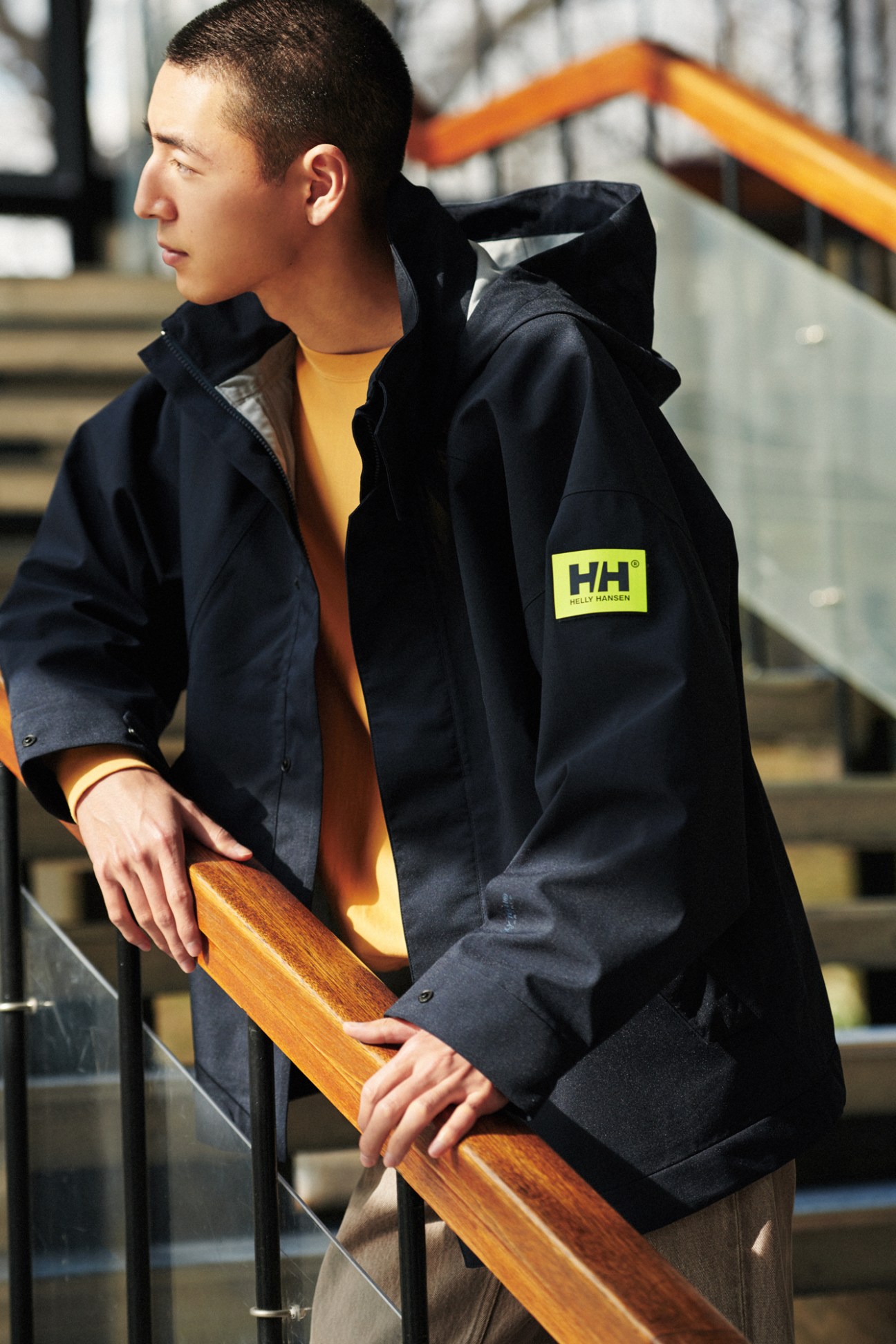 Man in Helly Hansen jacket and Auralee jumper and jeans leaning against wooden railing