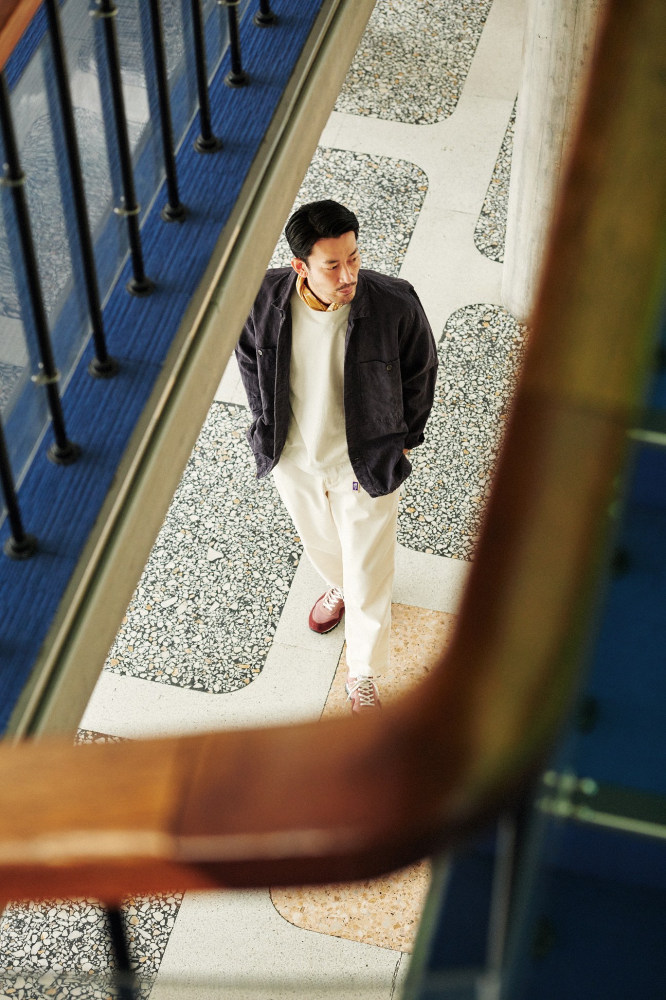 Man wearing Oliver Church jacket and The North Face Purple Label trousers standing on gravel courtyard viewed from above.