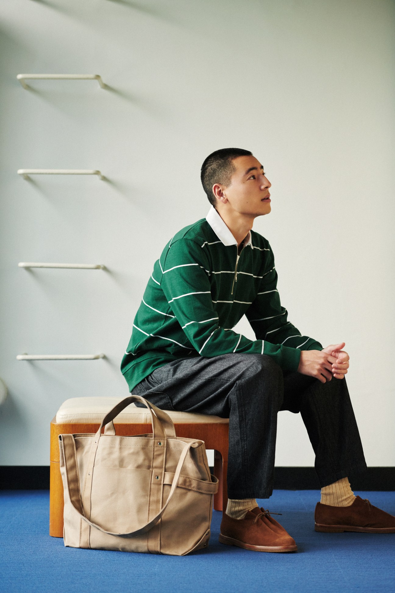 Man in green striped rugby shirt sitting on wooden bench with canvas bag on blue floor