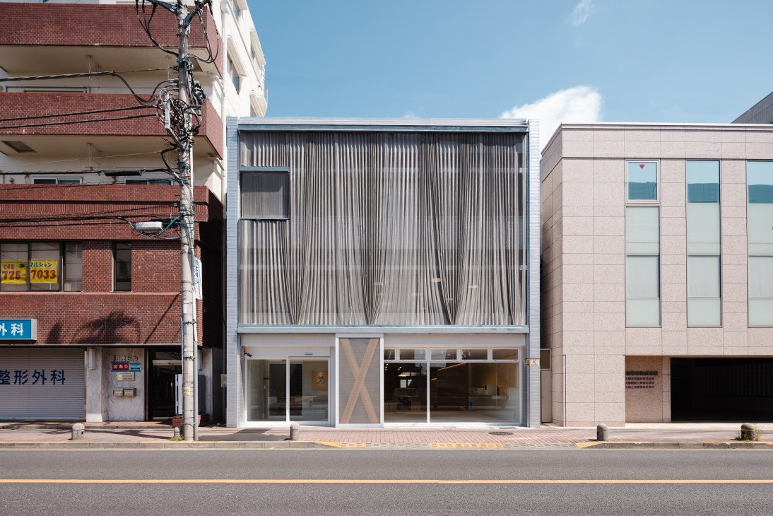 Modern building with a striking vertical wood-slatted facade situated between older brick and concrete structures on a sunny urban street.