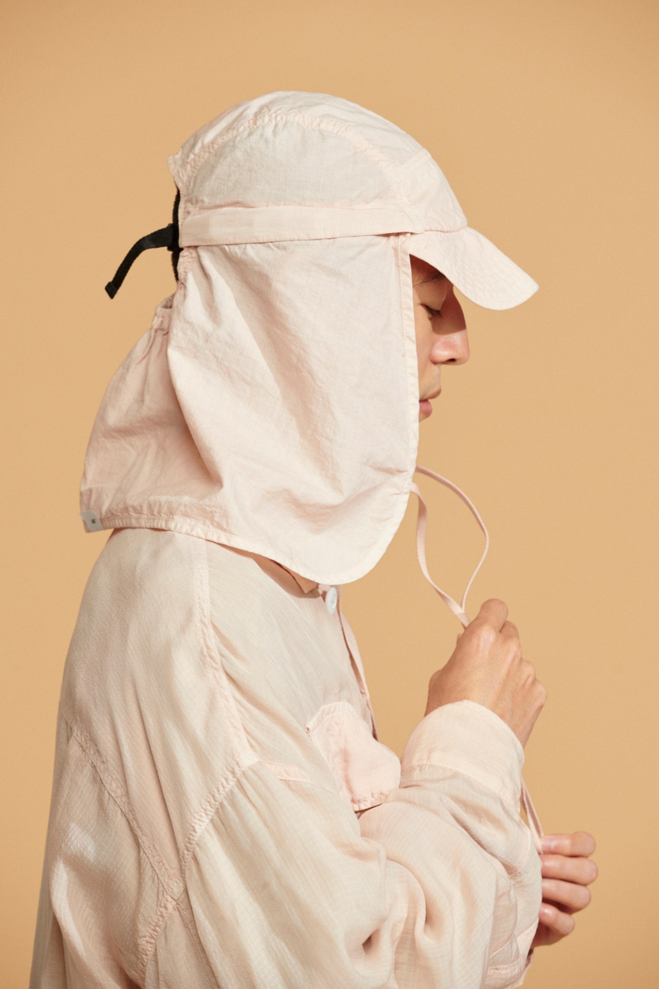 Model wearing beige Innat jacket and cap with face covering against neutral background