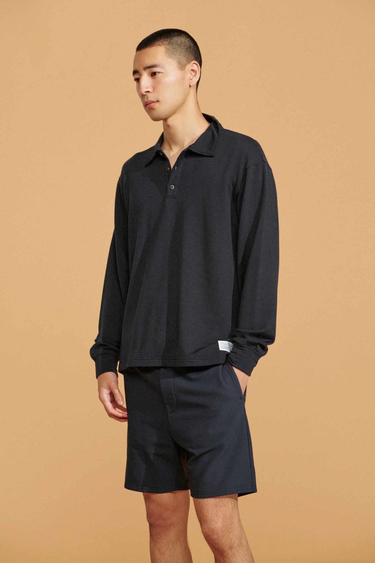Model in navy long-sleeve polo shirt and navy shorts against beige background