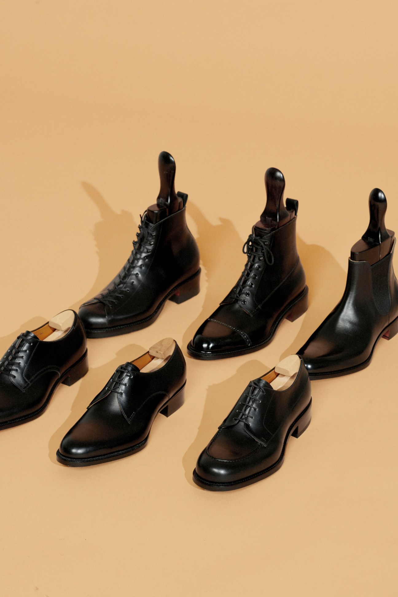 Collection of black leather dress shoes and boots by Takeshi Mori arranged on beige background