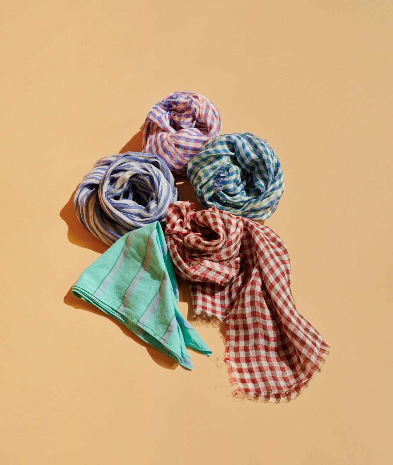 Five colorful checkered and striped scarves arranged on tan background