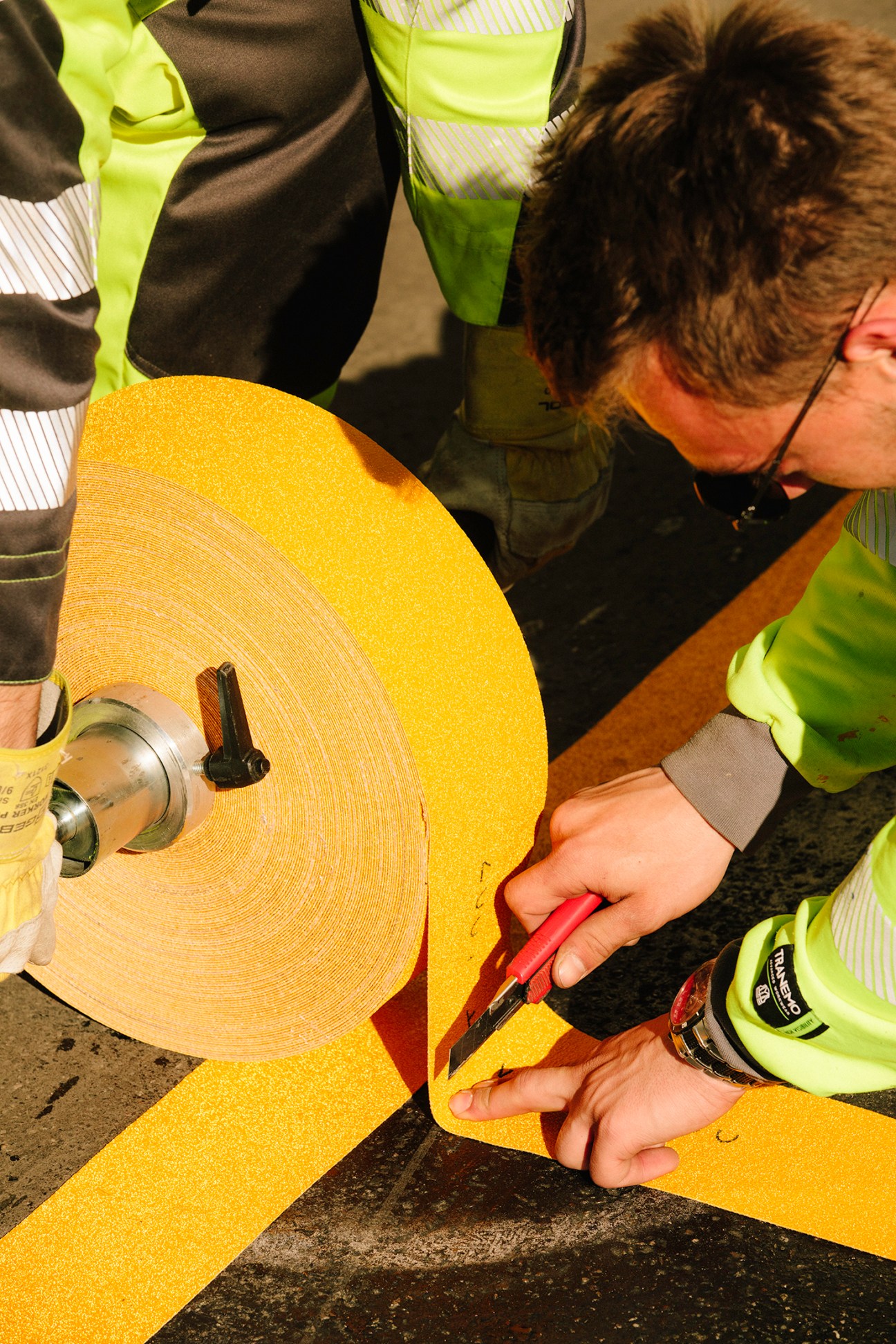 Workers in high-visibility vests applying bright yellow tape to a road surface during lockdown.