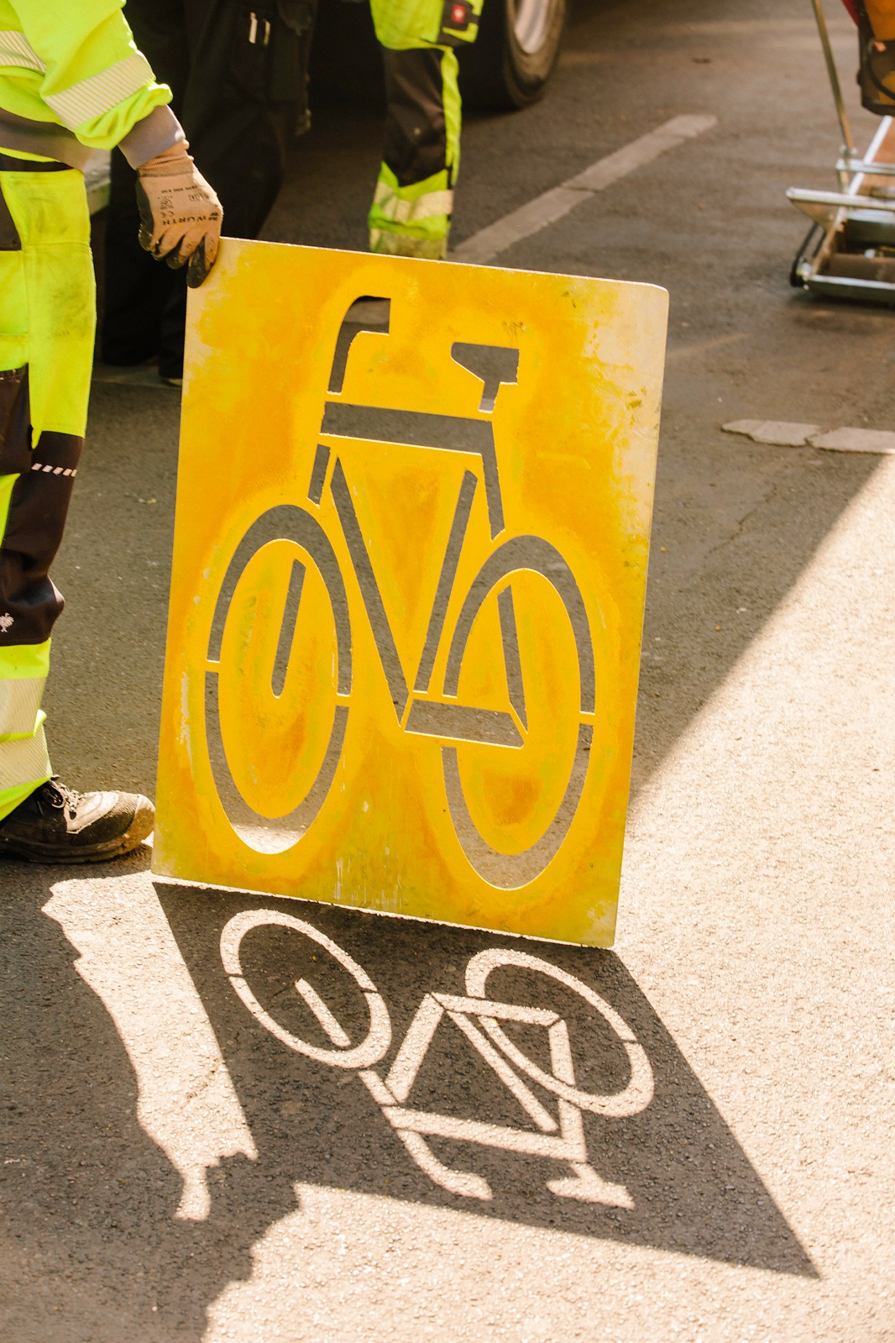 Worker in high-visibility clothing holding a yellow bicycle lane sign on a Berlin street.