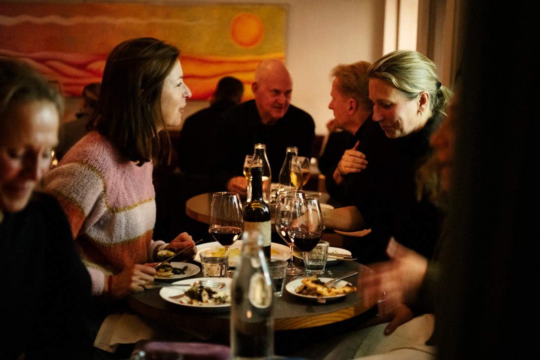 People dining at a restaurant table with wine glasses, plates of food, and warm lighting
