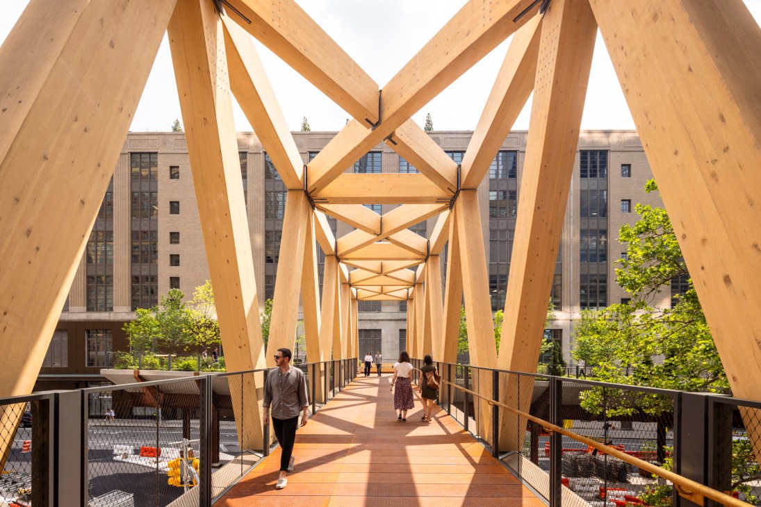 People walking across a modern wooden pedestrian bridge with geometric timber arches and metal railings