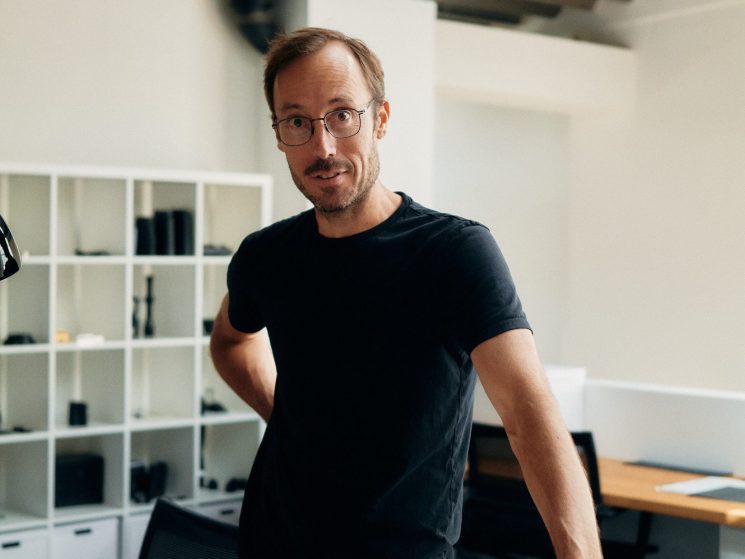 Mark Shipard, head of design at Leica Camera AG, standing at a white desk with camera components in an office
