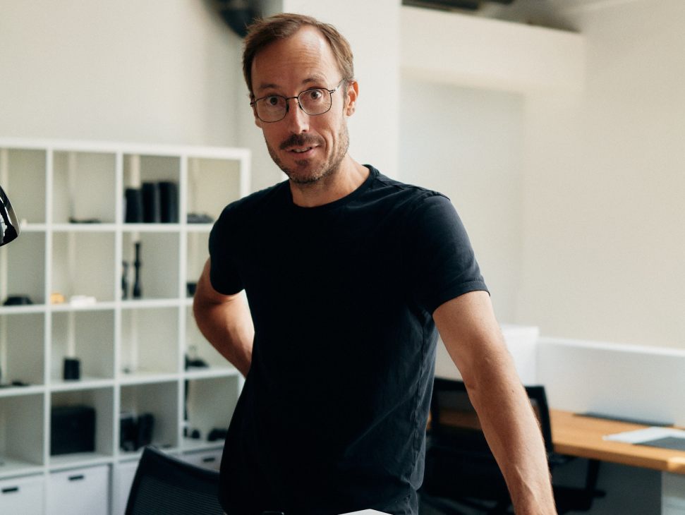 Mark Shipard, head of design at Leica Camera AG, standing at a white desk with camera components in an office