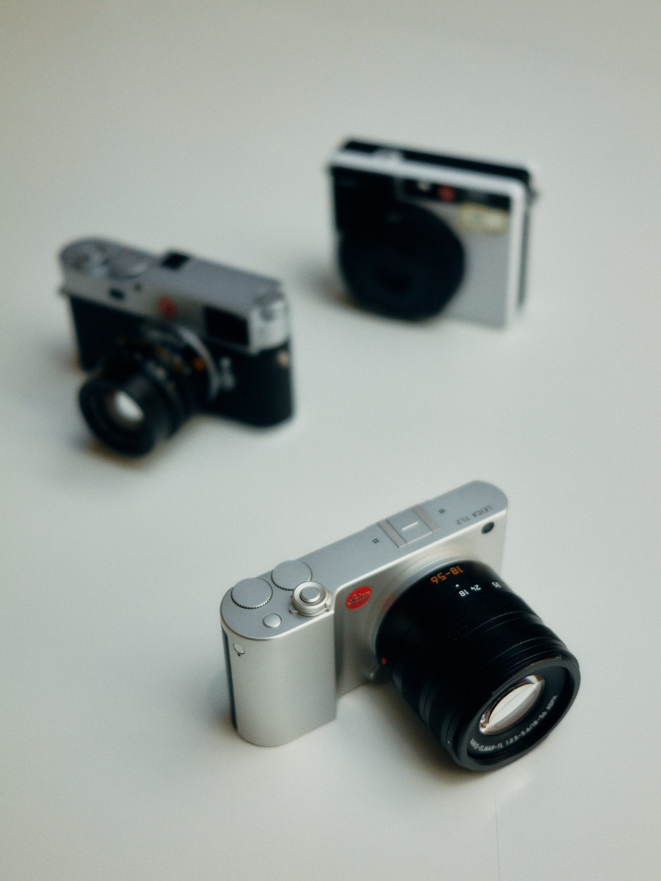 Three Leica cameras displayed on a white surface showing different models and designs