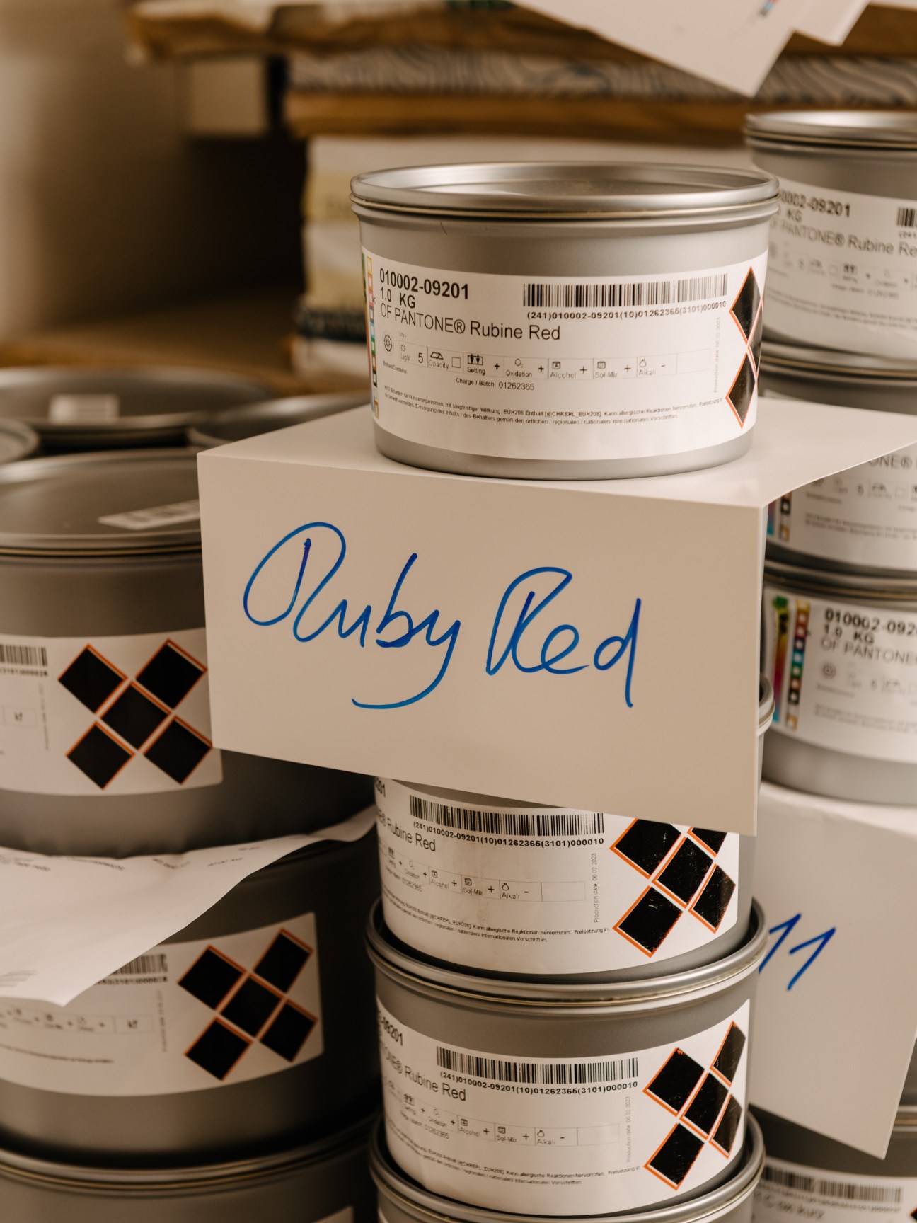 Stacked ink cans labeled with Pantone Ruby Red, with handwritten label identifying custom ink composition.