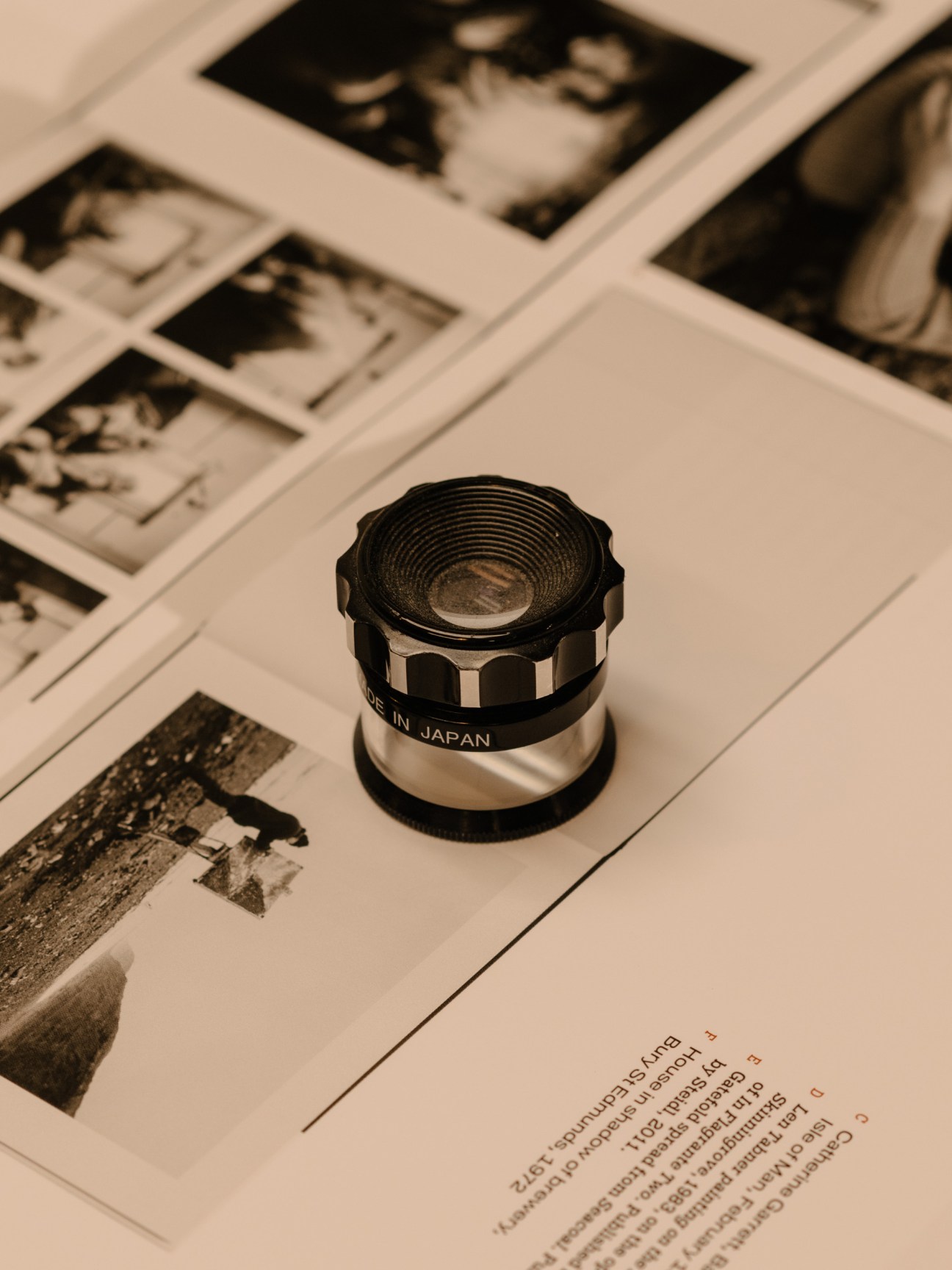 A magnifying loupe sits on printed photographs and text, used for quality control in book production.