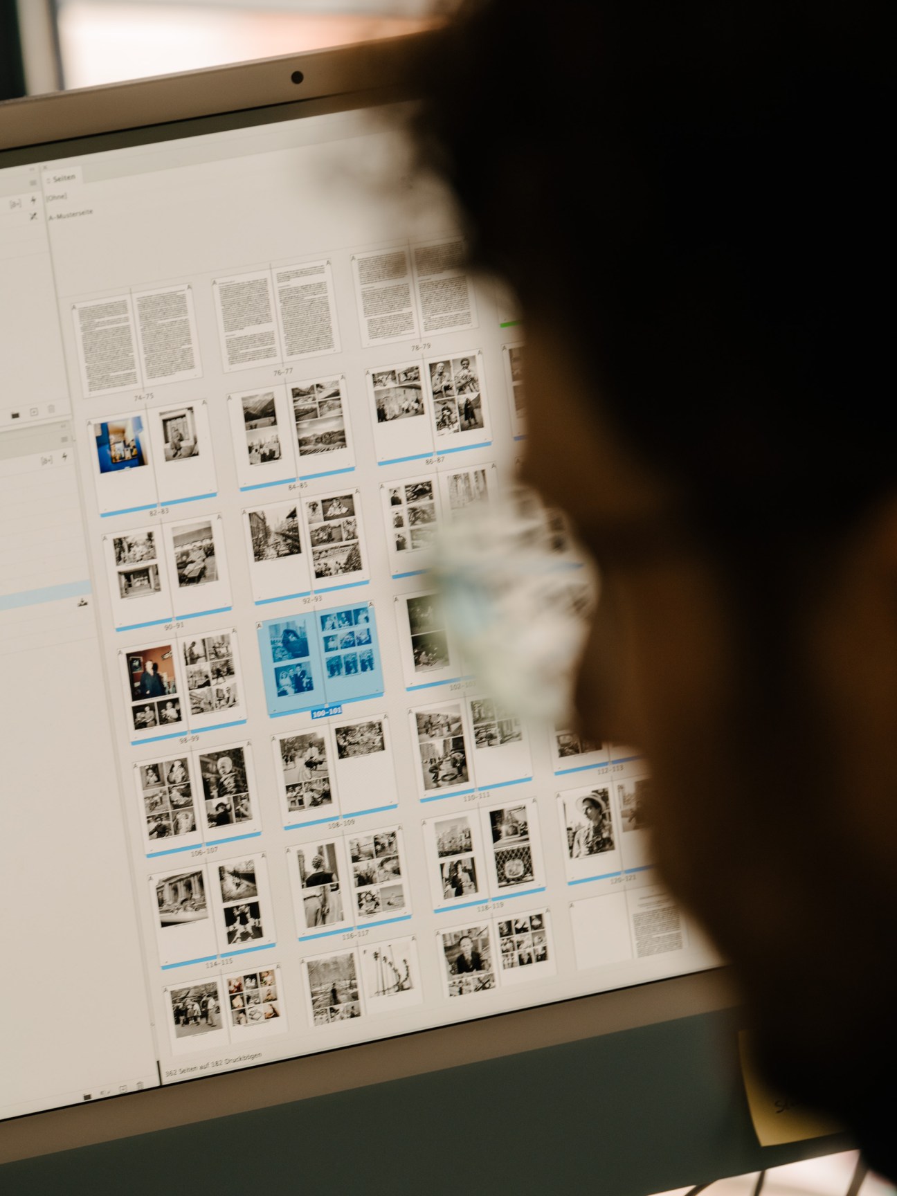 Person reviewing a printed layout sheet with multiple photographs and text sections displayed on a light table.