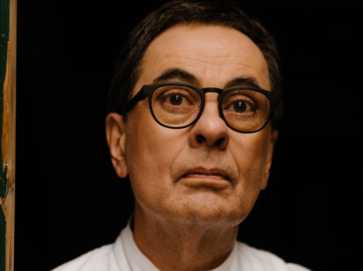 man with a serious expression in a white shirt holding a blue pen
